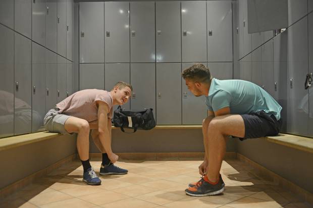 The image depicts two gentlemen having a conversation in what appears to be a locker room.